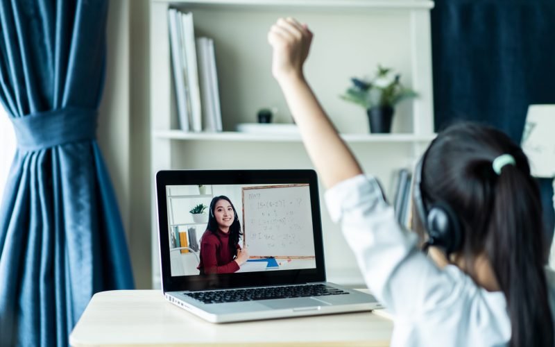 Homeschool Asian little young girl student learning virtual internet online class from school teacher by remote meeting due to covid pandemic. Female teaching math by using headphone and whiteboard.