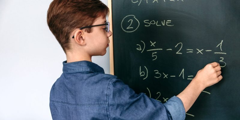 Boy solving math exercises on blackboard at school