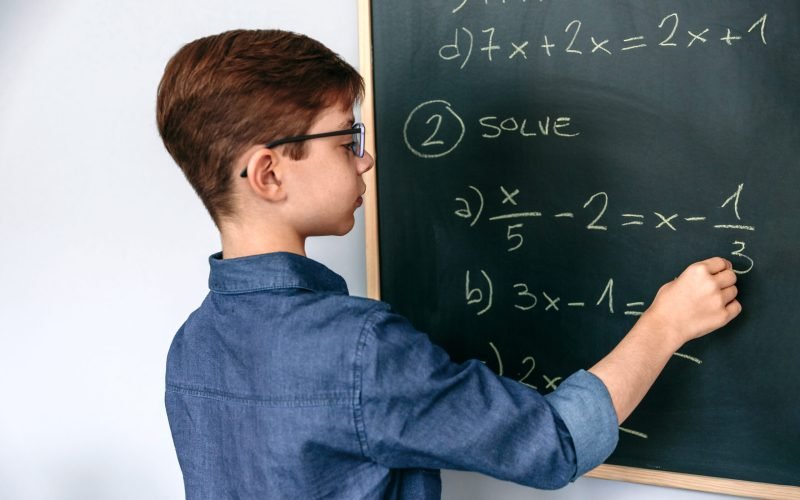 Boy solving math exercises on blackboard at school