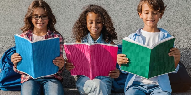 Close up of smiling school kids with backpacks holding notebooks and having fun outdoors