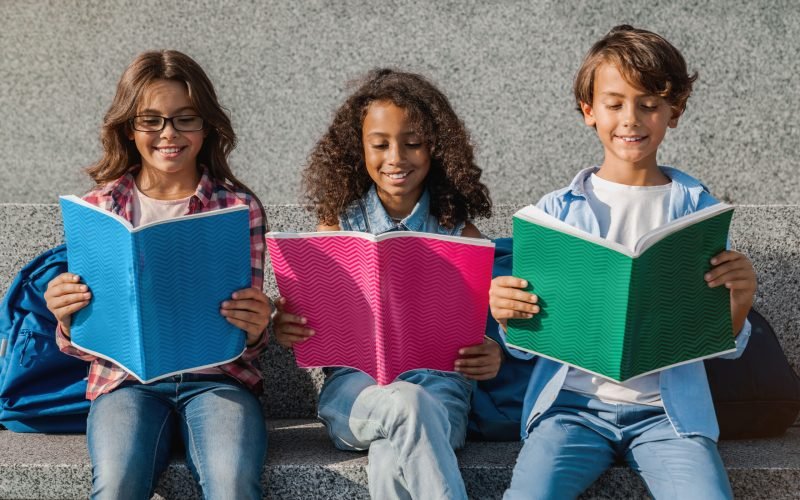 Close up of smiling school kids with backpacks holding notebooks and having fun outdoors