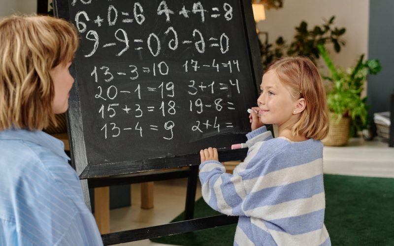 Proud girl holding white chalk and doing sums while looking at her mom