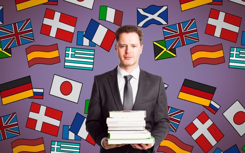 man-with-books-stacked-standing-before-flags-2026-03-26-05-05-39-utc
