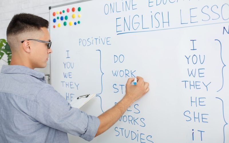 Online English school at home, webinar and new normal. Serious guy in glasses writes rules on blackboard and streams video for students during coronavirus pandemic, close up, free space