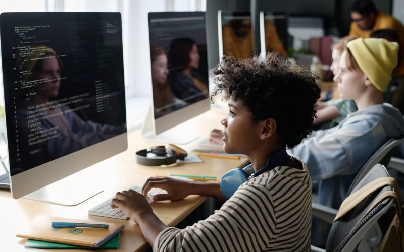Side view shot of African American teen boy coding on computer during modern IT class at school