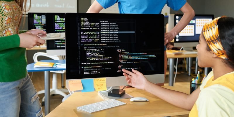 Group of students discussing computer codes on computer in team during IT lesson