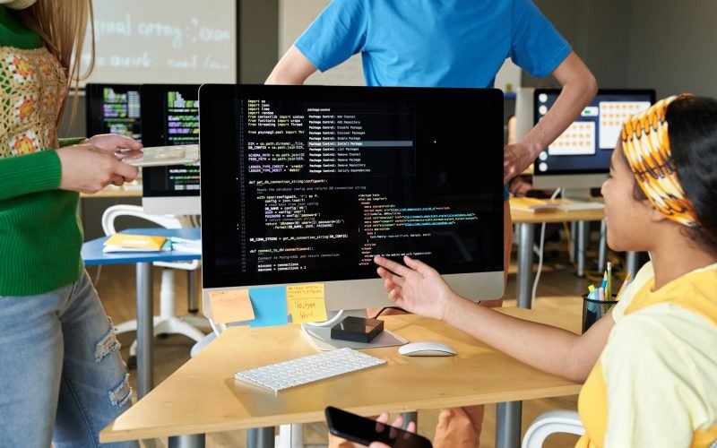 Group of students discussing computer codes on computer in team during IT lesson