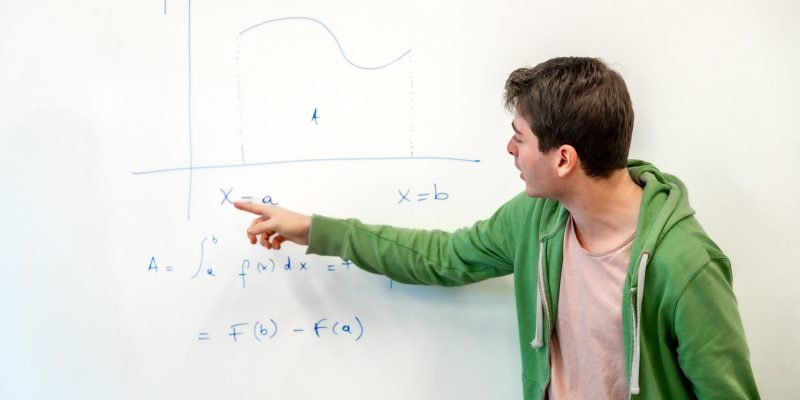 Young college student explaining a mathematical integral calculus formula, pointing at a graph on a whiteboard