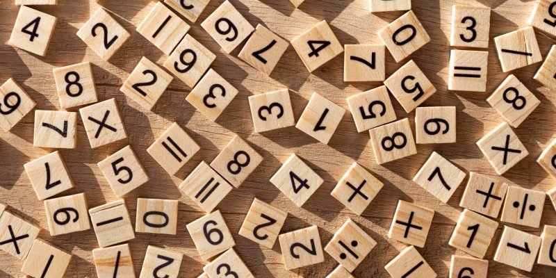 Scattered wooden plaques with numbers and signs. Flat lay. Teaching material in mathematics, Montessori method. School background. Problem solving concept. Laser cutting and printing on wood.
